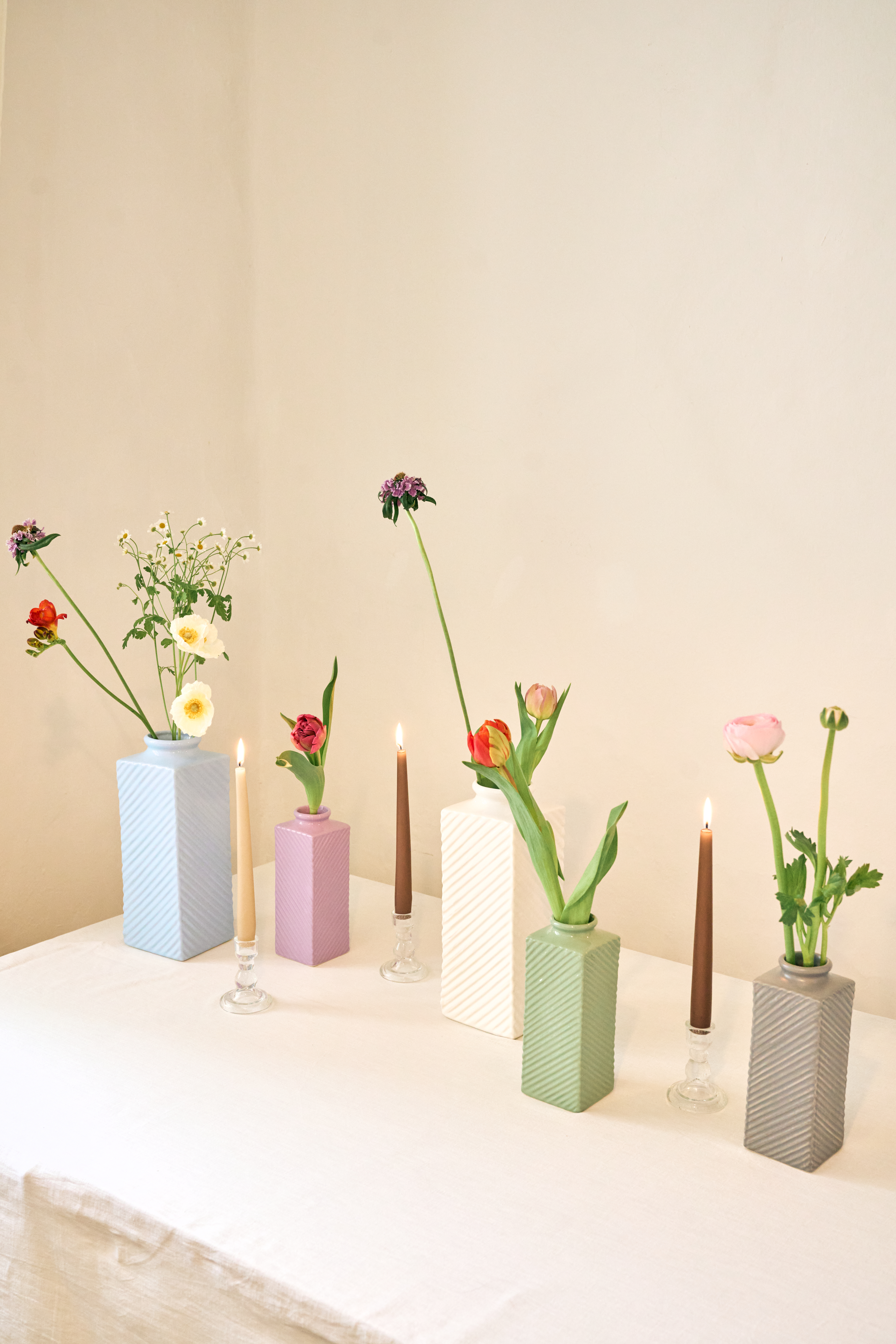 5 verschiedene Keramikvasen in 5 Farben und 3 Größen mit Blumen auf einem beigen Tisch