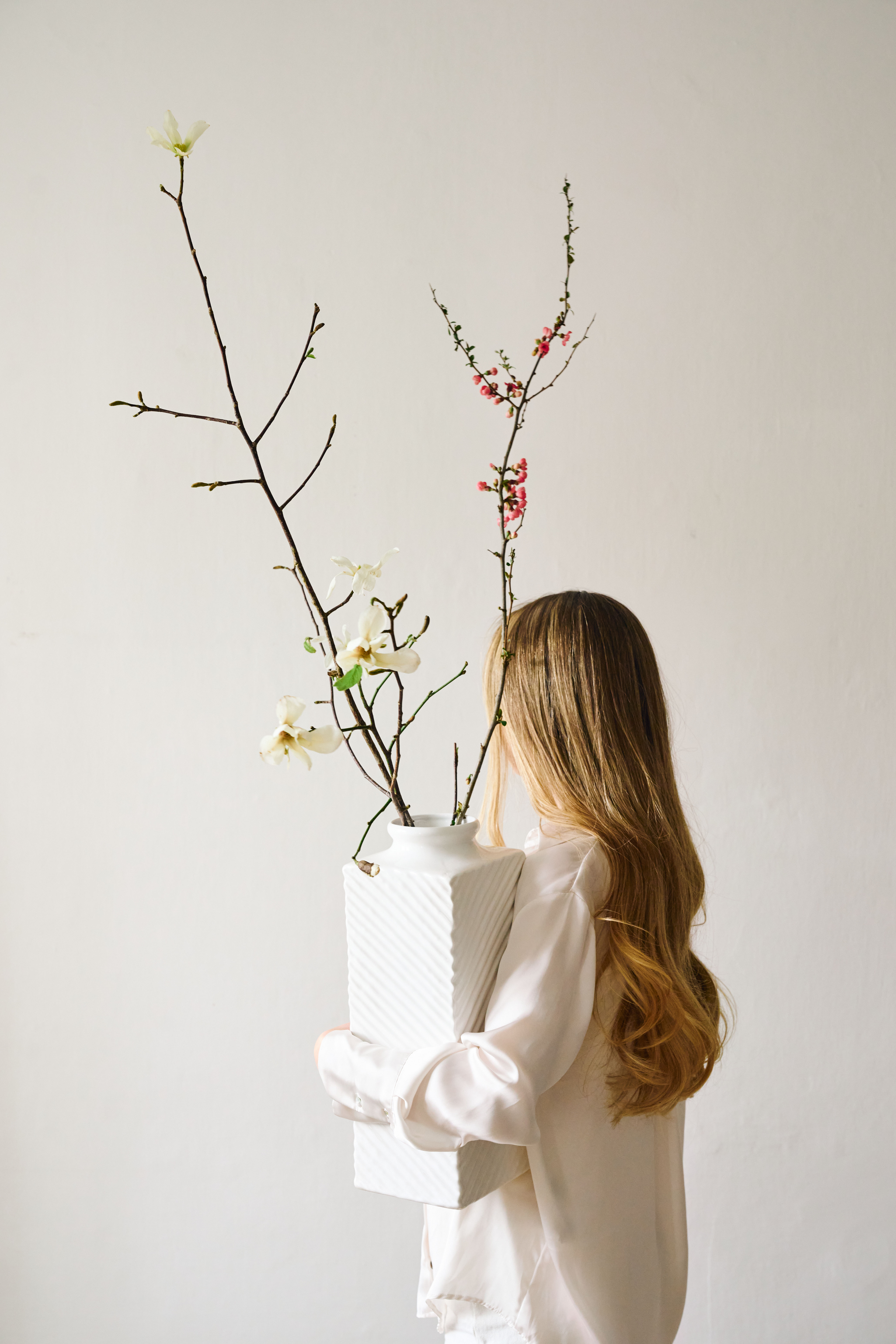 Eine Frau hält eine große Weiße Vase mit Blumen in der Hand