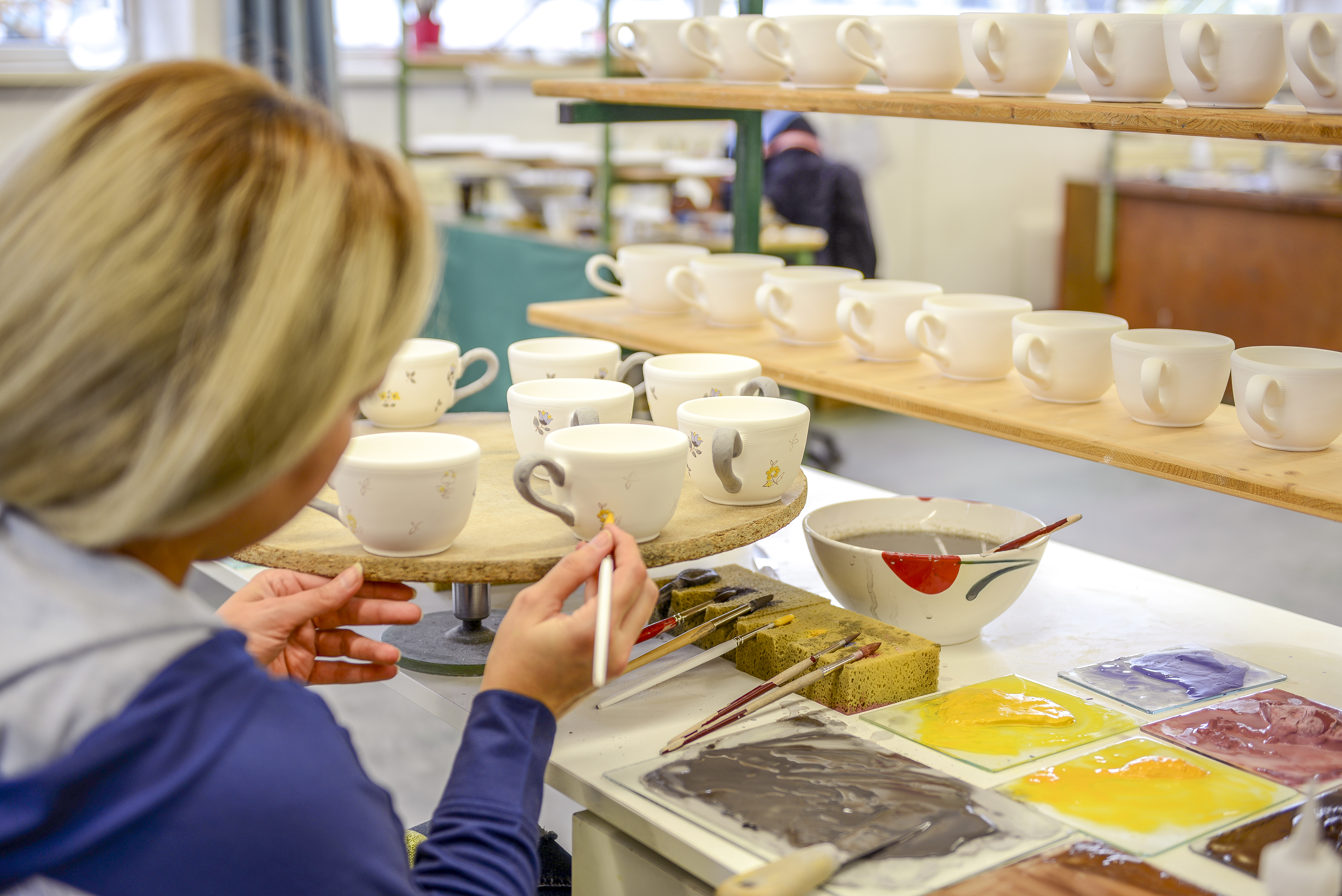 Eine Malerin bemalt Kaffeetassen im Streublumen Design