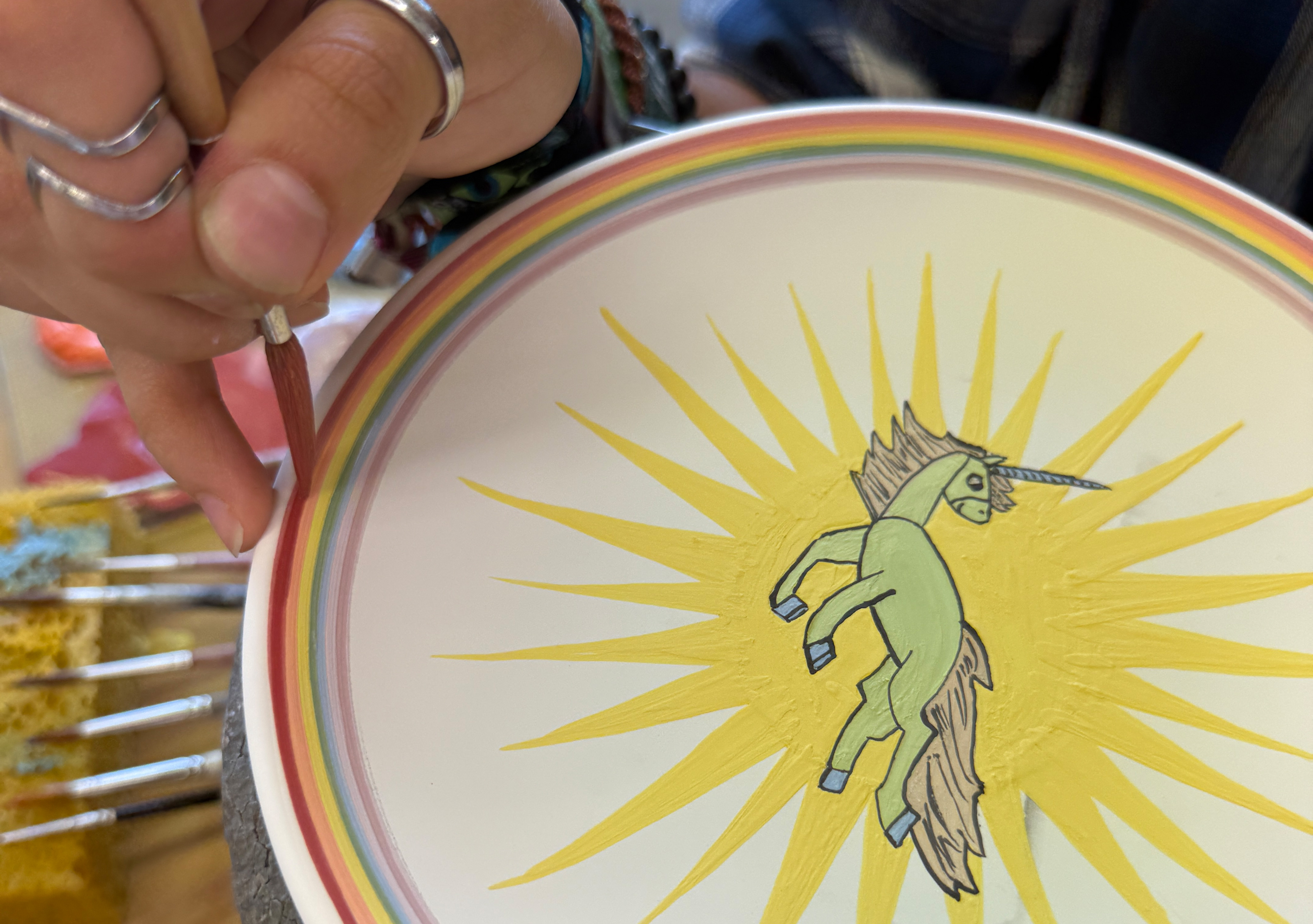 Eine Malerin bemalt den Rand eines Tellers in Regenbogenfarben