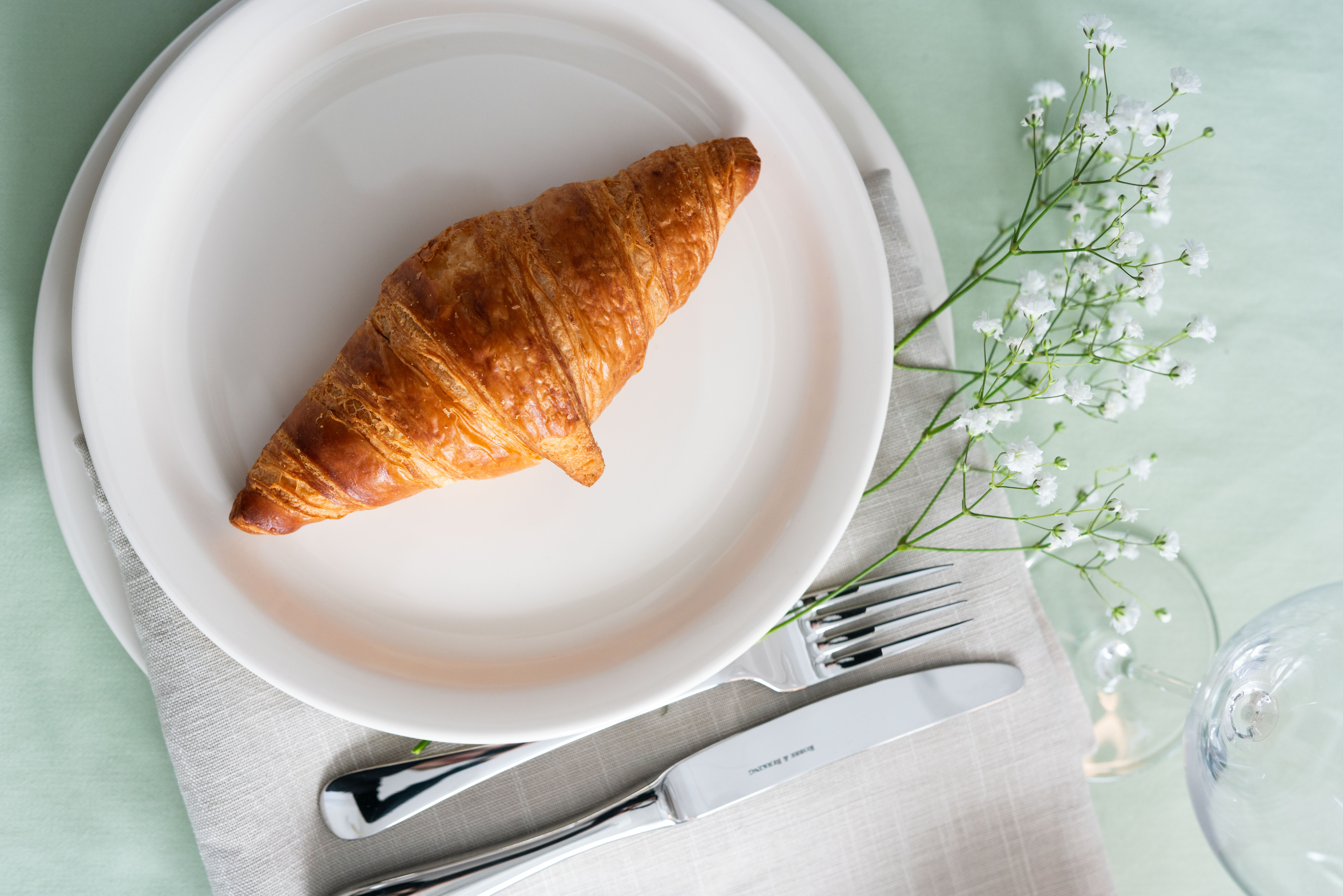 Ein Croissant auf einem weißen Teller auf einem Tisch mit einem grünen Tischtuch
