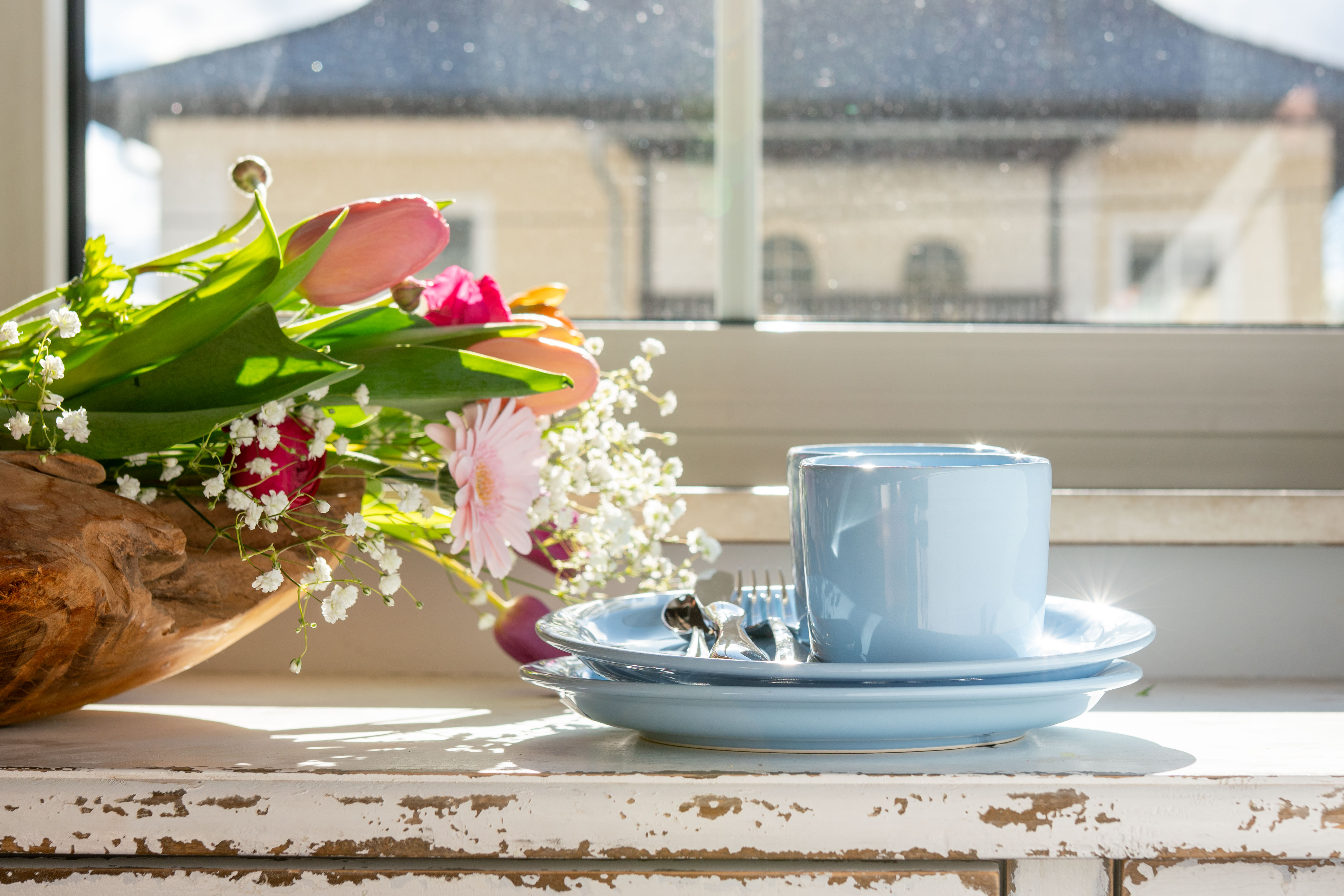 Blaue Teller und Tassen auf einem Regal neben Blumen