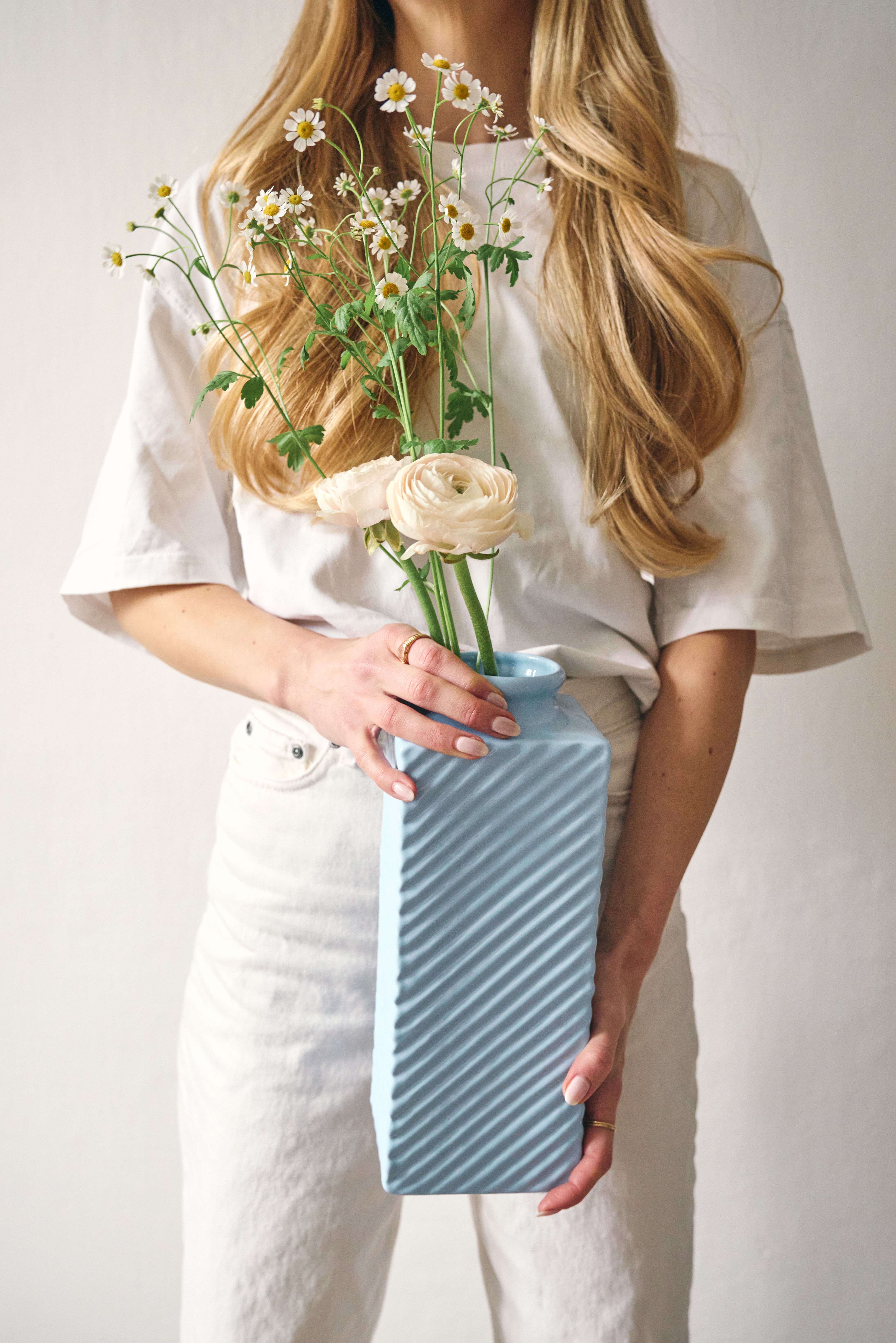 Eine Frau hält eine große Eisblaue Vase mit Blumen in den Händen