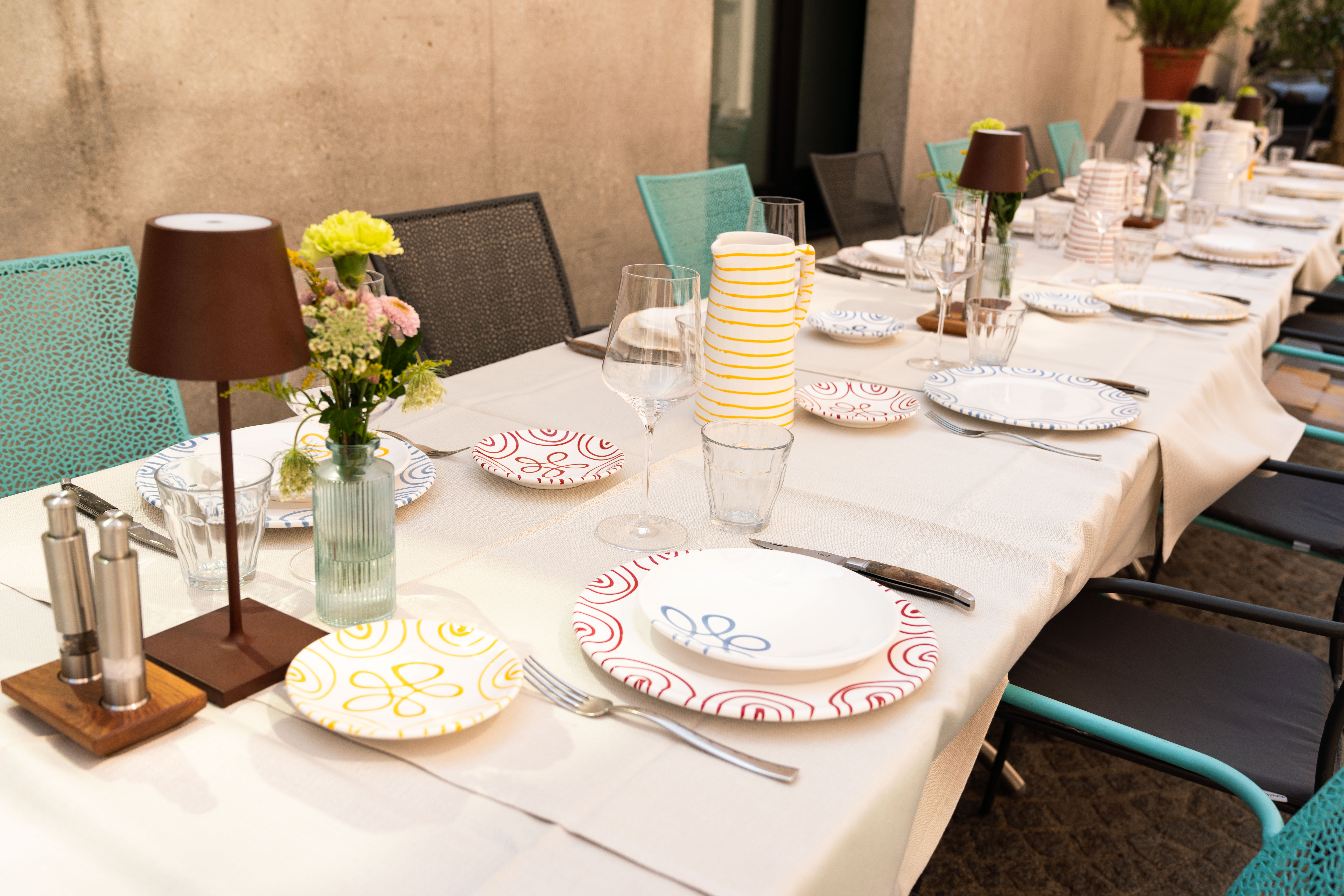 Ein Gedeckter Tisch mit Tellern in verschiedenen geflammten Designs und bunten Stühlen